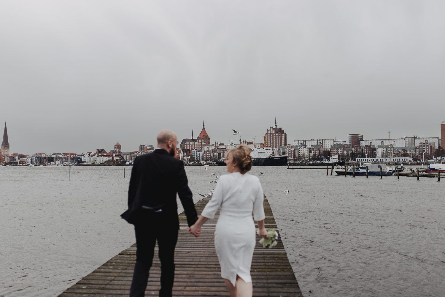 Aufgenommen von Hochzeitsfotograf Kupfergold Photographie aus Rostock. Zu sehen ist ein Foto eines Elopments im Rostocker Stadthafen.  Brautpaarshooting mit Skyline von Rostock im Hintergrund