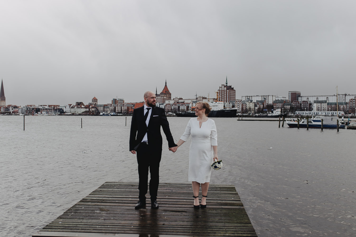 Aufgenommen von Hochzeitsfotograf Kupfergold Photographie aus Rostock. Zu sehen ist ein Foto eines Elopments im Rostocker Stadthafen.  Brautpaarshooting mit Skyline von Rostock im Hintergrund